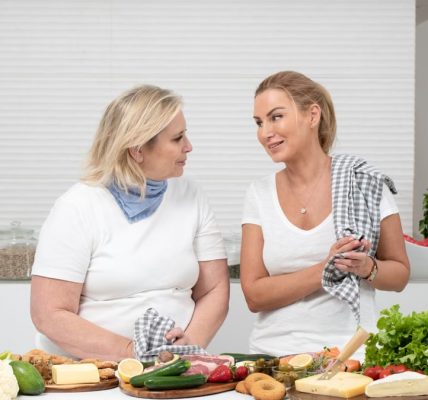 Two women in a kitchen preparing fresh vegetables and cheese with olive oil and spices.